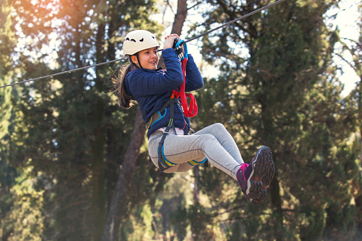 Happy school girl enjoying activity in a climbing adventure park on a sunny day