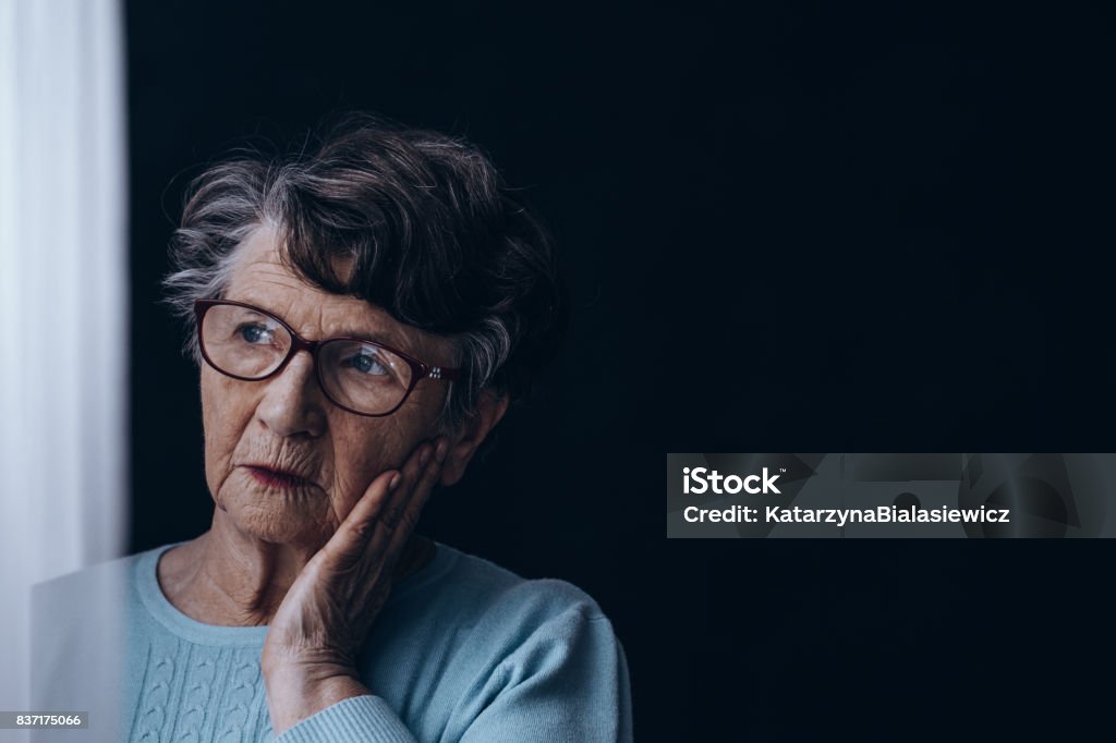 Old woman in dark room Sad, old woman standing alone in dark room Alzheimer's Disease Stock Photo