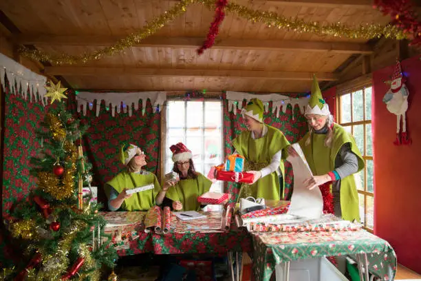 Four women dressed as Santa's elves wrap presents ready for Christmas.