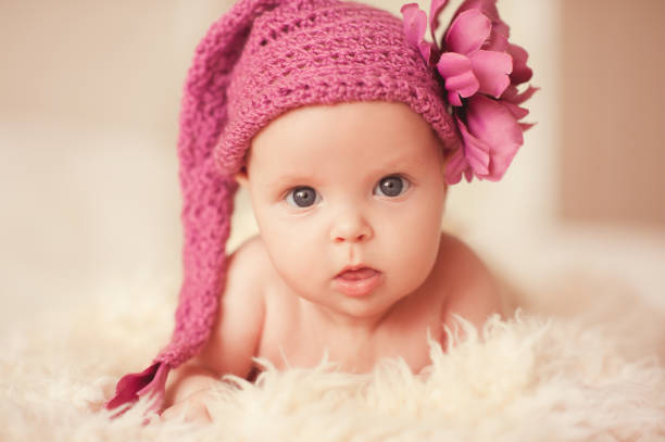 Cute baby girl 2-3 month old wearing knitted pink hat with decorative flower. Looking up. Childhood.