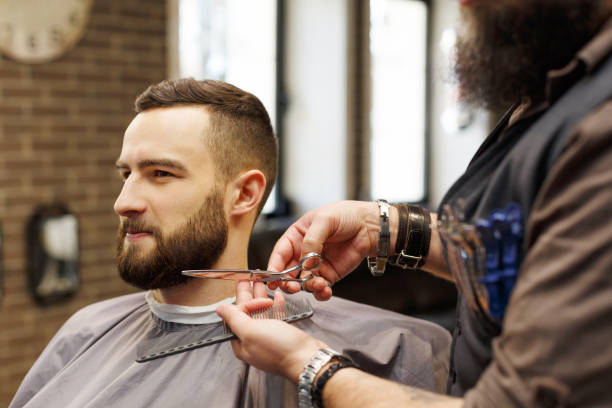 istock Barber styling beard with scissors to client at barbershop 837237298