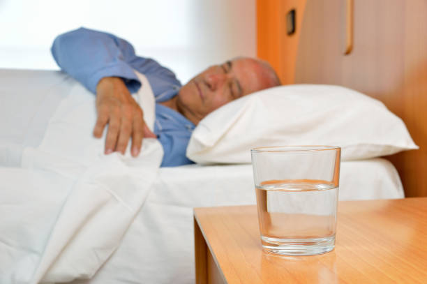 senior man sleeping with water Senior man lying on bed with glass of mineral water on the nightstand old man pajamas photos stock pictures, royalty-free photos & images