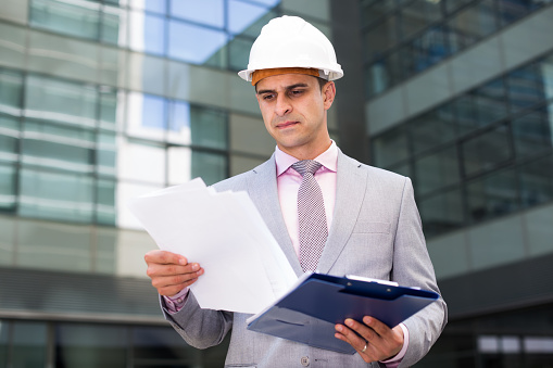 Portrait of concentrated businessman reading documents outdoor on factory background