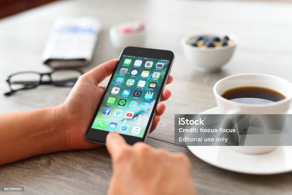 Using Apple iPhone 6 İstanbul, Turkey - August 15, 2017: Woman using smart phone on a wooden desk. The smart phone is an iPhone 6 plus.  iPhone is a touchscreen smartphone developed by Apple Inc. iPhone Stock Photo