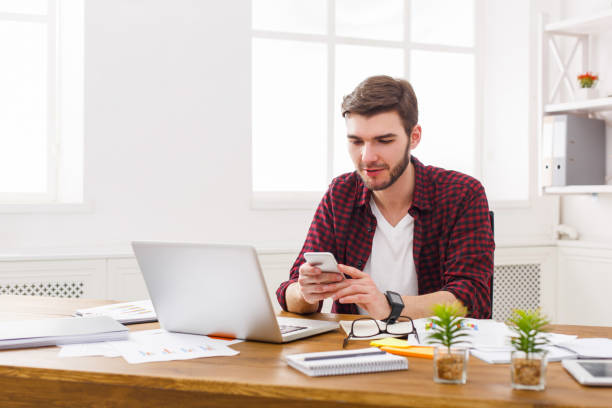 istock Young businessman in office using cell phone by the laptop 837308602