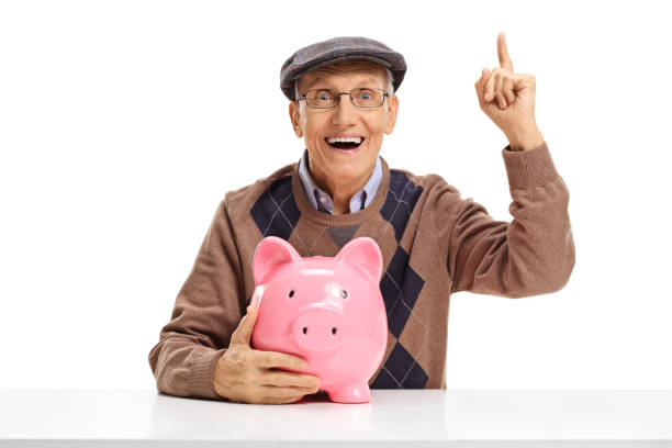 istock Cheerful senior with piggybank at a table pointing up 837325868