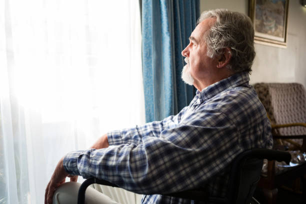 istock Senior man looking through window while sitting on wheelchair in retirement home 837338706