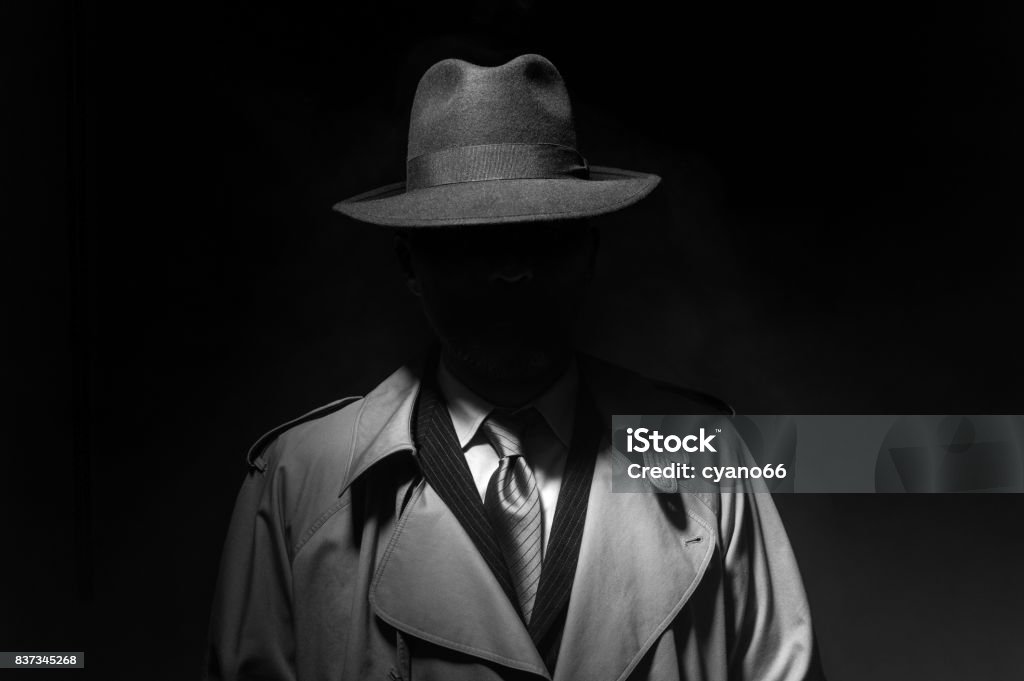 Noir movie character Man posing in the dark with a fedora hat and a trench coat, 1950s noir film style character Spy Stock Photo