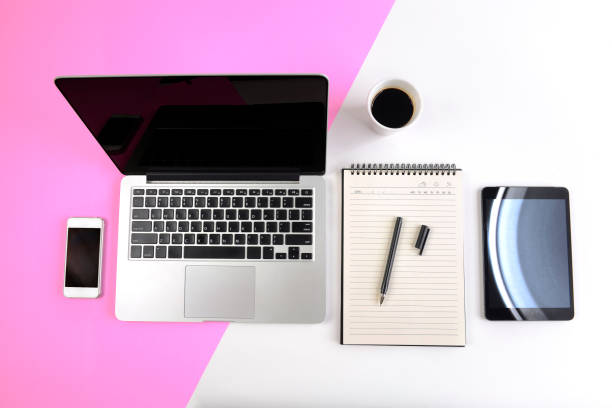 Office table with  laptop computer, notebook, digital tablet and smartphone on modern two tone (white and pink) background.