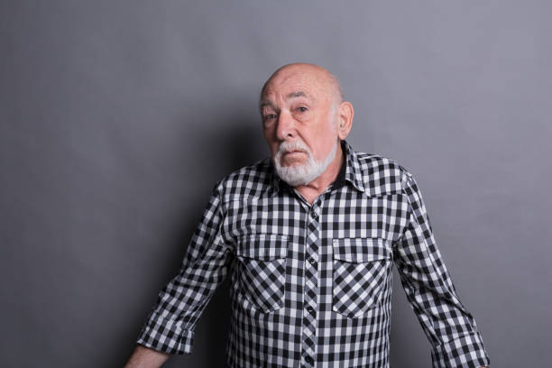 Portrait of confused senior man Portrait of unsure senior man looking confused, gray studio background confusion raised eyebrows human face men stock pictures, royalty-free photos & images