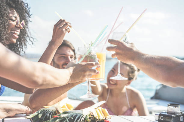szczęśliwi przyjaciele pijący tropikalne koktajle na imprezie łodzi i jedzący ananasa - młodzi ludzie bawiący się na wycieczce morskiej - koncepcja młodzieży i lata - główny nacisk na lewe dolne szkło - filtr retro - cruise ship cruise beach tropical climate zdjęcia i obrazy z banku zdjęć