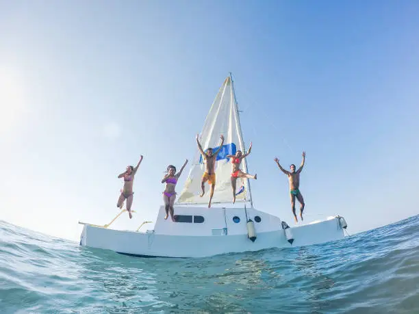 Happy friends jumping off the catamaran boat into the ocean - Young people having fun diving into the sea - Travel, tropical, summer and concept - Soft focus on center guys - Fisheye lens distorsion