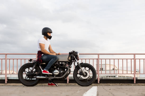 Brutal man sit on cafe racer custom motorbike. Handsome happy rider man in red sneakers, white t-shirt and black moto helmet sit on his classic style biker cafe racer motorcycle. Bike custom made in vintage garage. Brutal fun urban lifestyle. cafe racer stock pictures, royalty-free photos & images