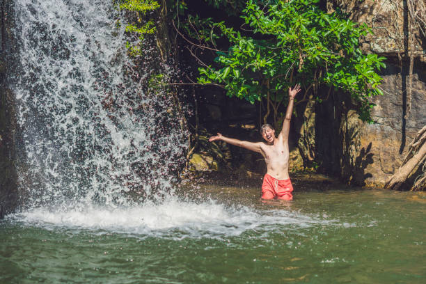 istock Side view of young man with arms standing against waterfall 837430486
