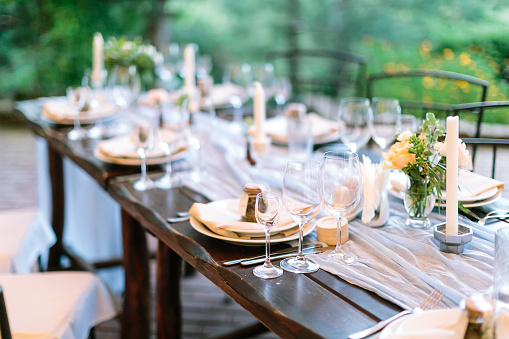 fest, dinner, tradition concept. long oaken table served for celebration with silverware, dishes and transparent dazzling glasses, flowers and candles in interesting holders in form of octagonal