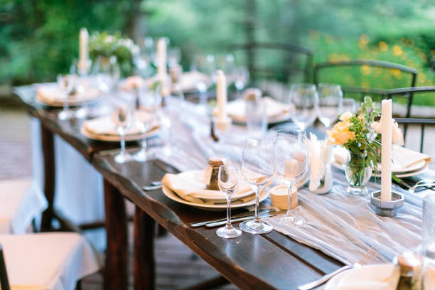 fest, dinner, tradition concept. long oaken table served for celebration with silverware, dishes and transparent dazzling glasses, flowers and candles in interesting holders in form of octagonal stock photo