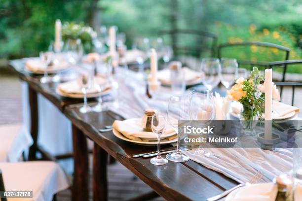 Fest Dinner Tradition Concept Long Oaken Table Served For Celebration With Silverware Dishes And Transparent Dazzling Glasses Flowers And Candles In Interesting Holders In Form Of Octagonal Stock Photo - Download Image Now