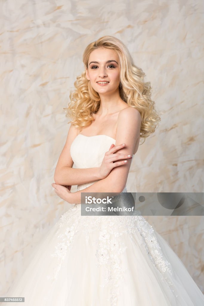 Fashionable White Gown Beautiful Blonde Model Bride Hairstyle And Makeup  Concept Young Smiling Girl In Wedding Festive Dress Standing Indoors On  Light Background Slender Woman Look Forward Stock Photo - Download Image