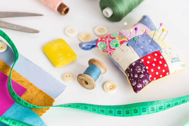closeup sewing tools , patchwork, tailoring and fashion concept - working environment on a white table, thread spools, buttons, meter, pincushion, scissors, pieces of colored patchwork fabric, soap stock photo