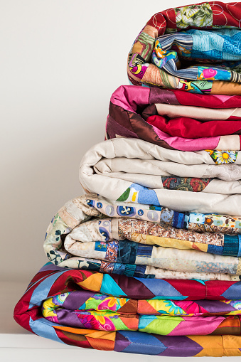sewing and fashion concept - closeup stack of colorful quilts, beautiful bedspreads stacked in several rows in height for storage, sale patchwork productions on white background, copy space, vertical