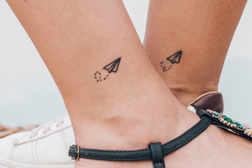 Two friends having the same tattoo in their ankles.