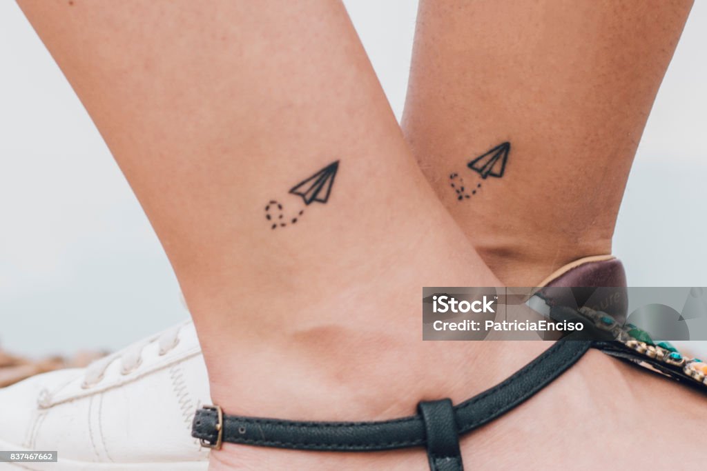 Two women having the same tattoo Two friends having the same tattoo in their ankles. Tattoo Stock Photo