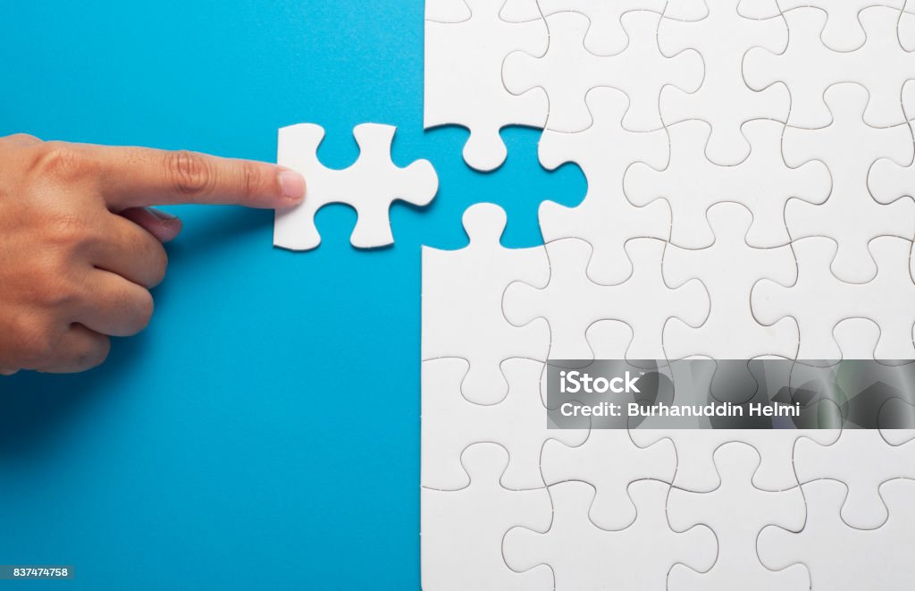 Mano que sostiene la pieza de puzzle blanco sobre fondo azul. - Foto de stock de Rompecabezas libre de derechos