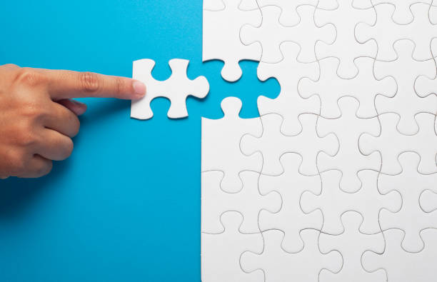 mano que sostiene la pieza de puzzle blanco sobre fondo azul. - jigsaw piece puzzle jigsaw puzzle metal fotografías e imágenes de stock