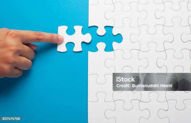 Mano Que Sostiene La Pieza De Puzzle Blanco Sobre Fondo Azul Foto de stock y más banco de imágenes de Rompecabezas