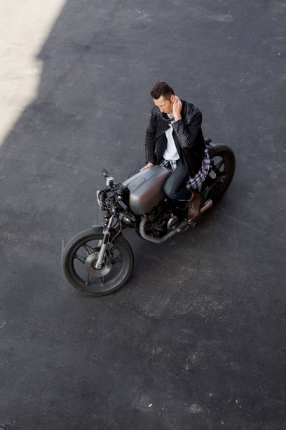 Top view to brutal man with cafe racer custom motorbike. Top view of a handsome rider man in black biker jacket and checkered shirt prepare for travel on classic style cafe racer motorcycle. Bike custom made in vintage garage. Brutal fun urban lifestyle. cafe racer stock pictures, royalty-free photos & images