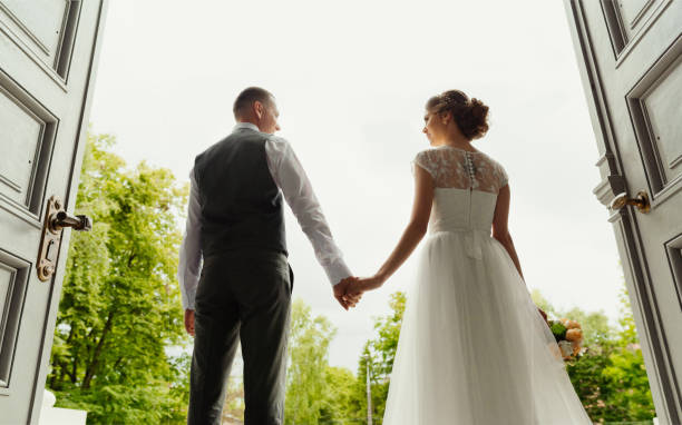 de la boda. día de la boda. pareja de boda. hermosa pareja, la novia y el novio miran y toman de la mano, contra el fondo de la salida de la catedral (portones altos) - young women wedding married engagement ring fotografías e imágenes de stock