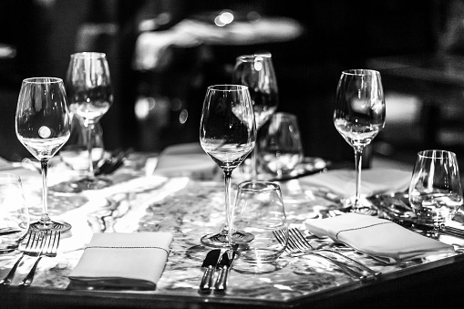 Black and white image of very large wine glasses placed on dinner table