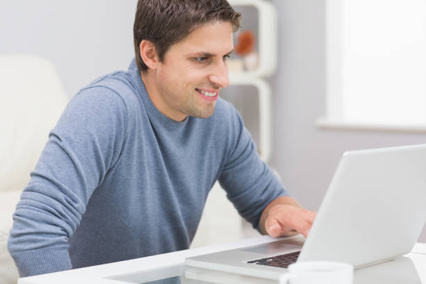 istock Smiling young man using laptop in living room 837544922
