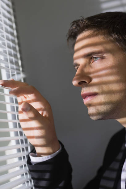 istock Serious young businessman peeking through blinds in office 837545870