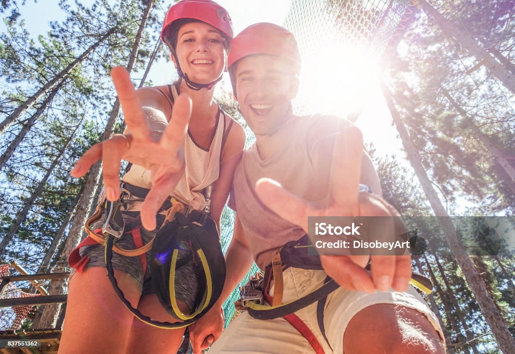 Couple of happy climbers having fun in adventure park outdoor - Young friends doing extreme sport - Travel,wanderlust and summer vacation - Focus on faces - Warm filter Climbing Stock Photo