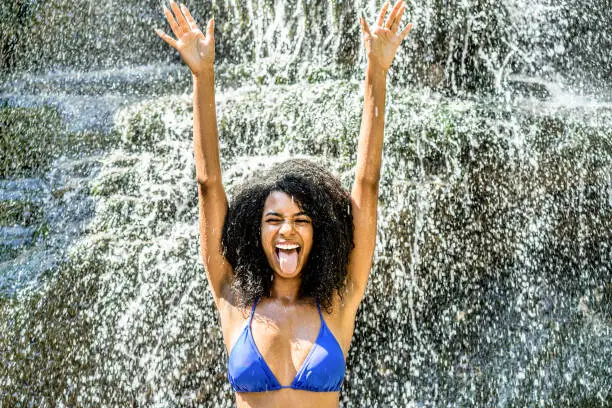 Photo of Young african descent woman having fun under river waterfalls - Handsome girl swimming with bikini in summer vacation - Youth, travel, tropical and rebel concept - Soft contrast filter