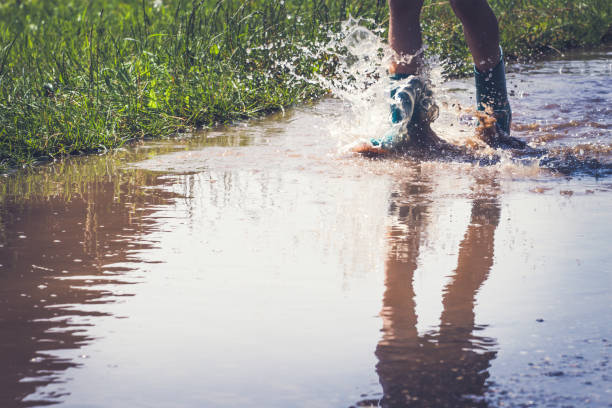 istock Legs of child in rainboots running through puddle 837581234
