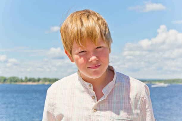 Portrait of squint blond boy in a white shirt near river