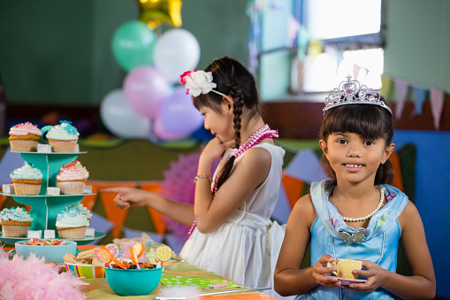 Cute girl having tea at table during birthday party at home