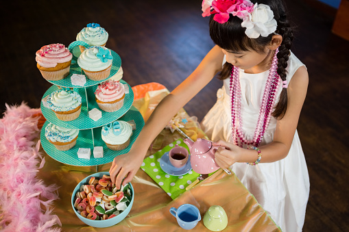 Girl having tea and confectionery at table during birthday party at home
