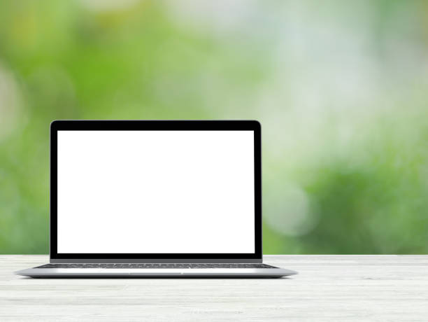 Laptop with blank screen placed on white wooden table in blurred green nature background stock photo