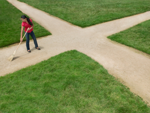 Woman sweeping dirt crossroad with broom surrounded by grass