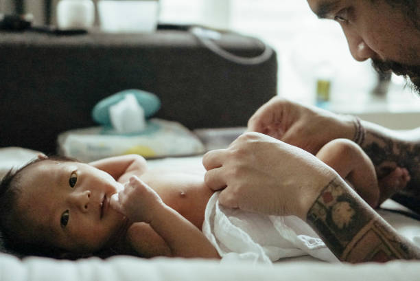 padre che cambia bambino (0-1 mesi) a letto - tattoo father family son foto e immagini stock
