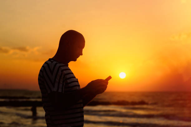 istock Man with phone in the background of the setting sun 837780772