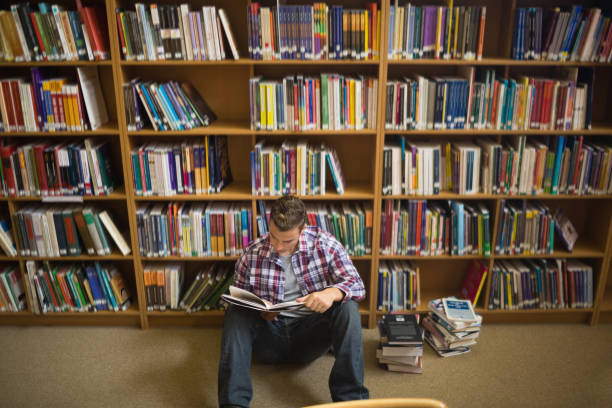 istock Concentrating young student sitting on library floor reading 837803378