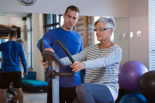 Physiotherapist showing workout record on exercise bike Physiotherapist showing workout record on exercise bike in clinic man 60s bicycle stock pictures, royalty-free photos & images