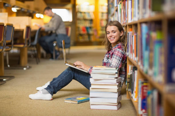 istock Smiling student using laptop on library floor looking at laptop 837834326
