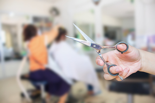 Hairdresser's hand hold scissors with salon beauty interior blur background