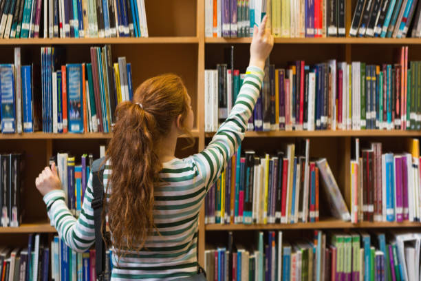 istock Redhead student taking book from top shelf in library 837835240