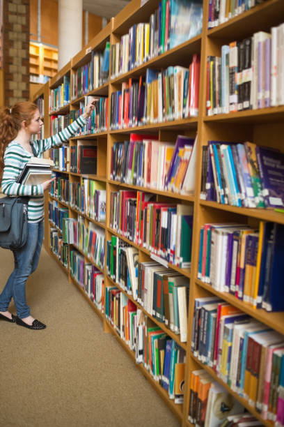 istock Redhead student taking book from bookshelf in the library 837836200